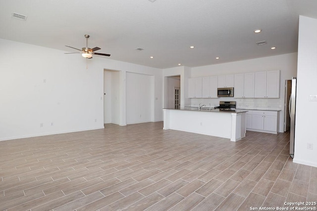 kitchen with ceiling fan, stainless steel appliances, tasteful backsplash, a kitchen island with sink, and white cabinets