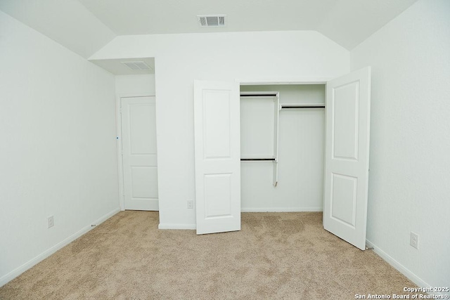 unfurnished bedroom with light carpet, a closet, and lofted ceiling