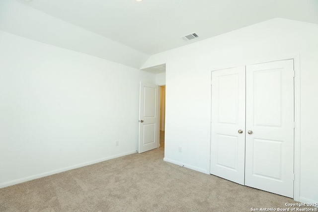 unfurnished bedroom featuring a closet, light colored carpet, and vaulted ceiling