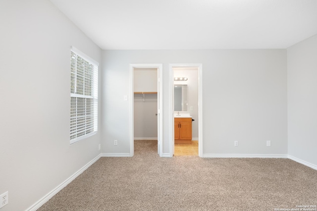 unfurnished bedroom with ensuite bathroom, sink, a spacious closet, light colored carpet, and a closet