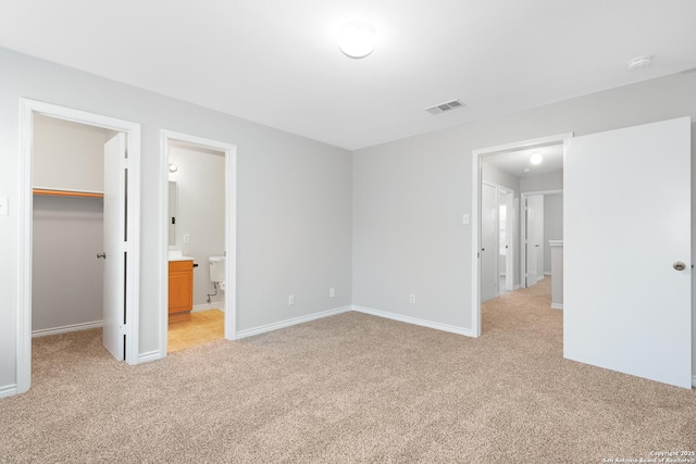 unfurnished bedroom with a spacious closet, light carpet, connected bathroom, and a closet