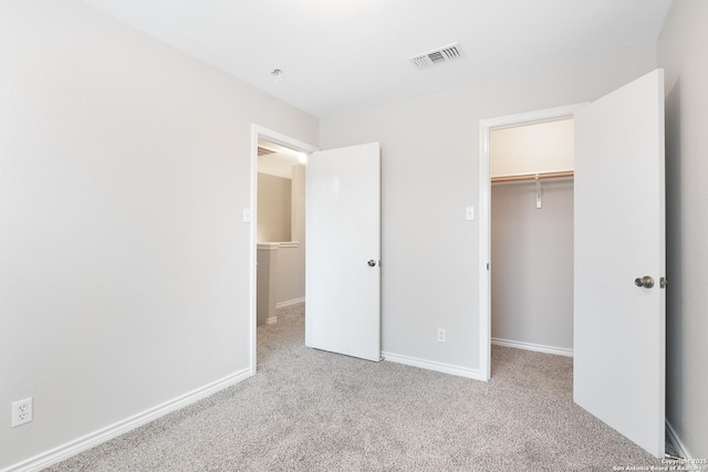 unfurnished bedroom with a spacious closet, a closet, and light colored carpet