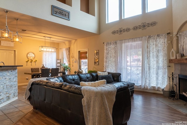 living room with a chandelier, hardwood / wood-style floors, a towering ceiling, and a stone fireplace