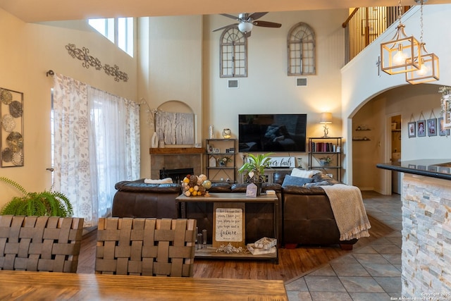 living room with tile patterned flooring, a towering ceiling, and ceiling fan with notable chandelier