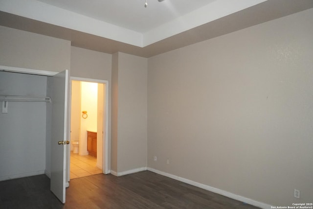 unfurnished bedroom with dark hardwood / wood-style flooring, a tray ceiling, and a closet