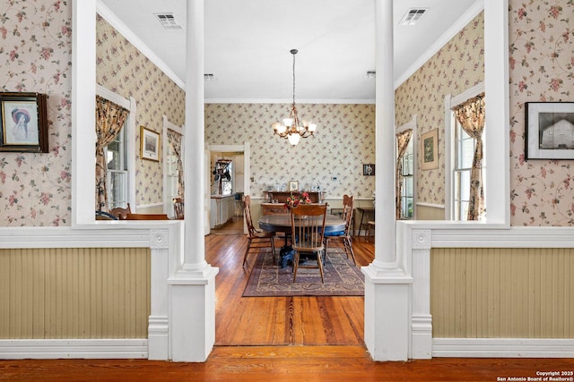 dining space with a chandelier, hardwood / wood-style floors, decorative columns, and crown molding