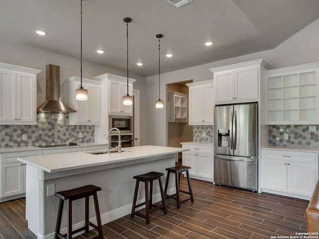 kitchen with white cabinetry, sink, wall chimney exhaust hood, stainless steel appliances, and decorative light fixtures