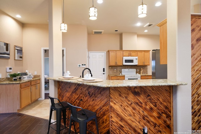 kitchen featuring light stone countertops, tasteful backsplash, kitchen peninsula, decorative light fixtures, and white appliances