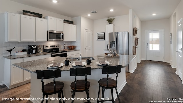 kitchen with light stone countertops, a breakfast bar, stainless steel appliances, white cabinetry, and an island with sink