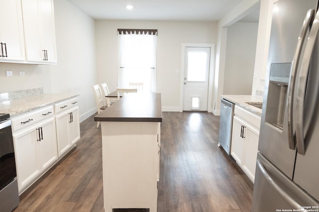 kitchen featuring light stone countertops, dark hardwood / wood-style flooring, stainless steel appliances, a kitchen island, and white cabinetry