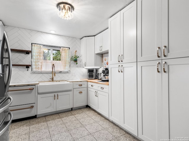 kitchen with backsplash, white cabinets, sink, light tile patterned floors, and stainless steel refrigerator