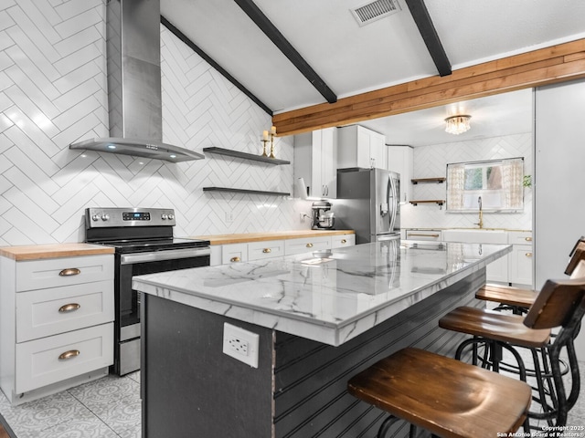 kitchen with white cabinets, appliances with stainless steel finishes, beamed ceiling, and wall chimney exhaust hood