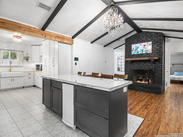 kitchen with sink, a brick fireplace, vaulted ceiling with beams, a kitchen island, and white cabinetry