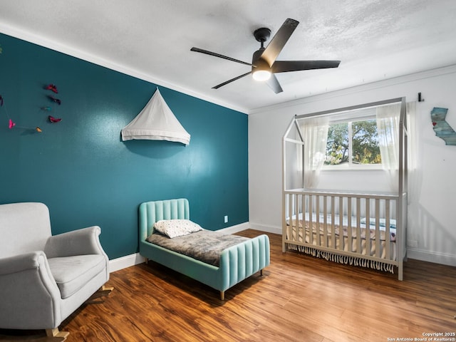 bedroom featuring ceiling fan, hardwood / wood-style floors, a crib, and ornamental molding