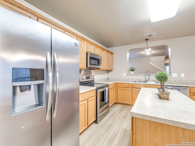 kitchen featuring sink, light brown cabinets, hanging light fixtures, stainless steel appliances, and light hardwood / wood-style flooring