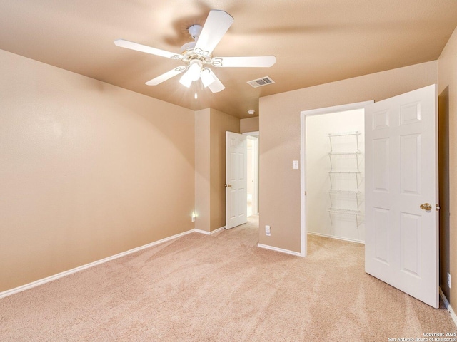 unfurnished bedroom with light carpet, a closet, a spacious closet, and ceiling fan