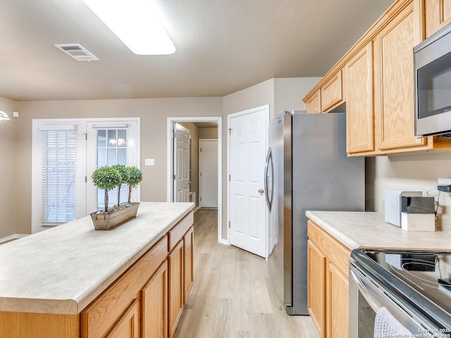 kitchen with light brown cabinets, light wood-type flooring, a textured ceiling, and appliances with stainless steel finishes