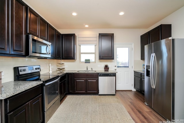 kitchen with sink, decorative backsplash, light stone countertops, light wood-type flooring, and appliances with stainless steel finishes