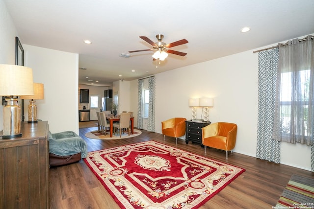 living room with a wealth of natural light, dark wood-type flooring, and ceiling fan