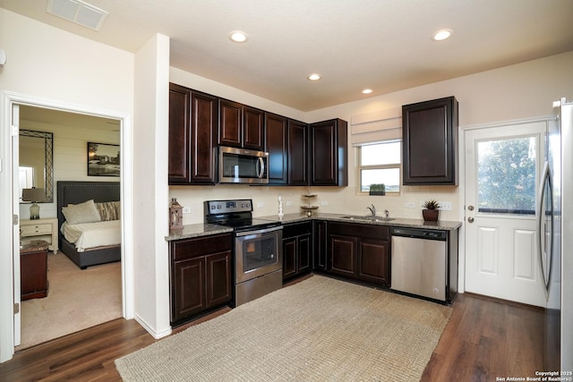 kitchen with appliances with stainless steel finishes, dark hardwood / wood-style flooring, light stone counters, dark brown cabinetry, and sink