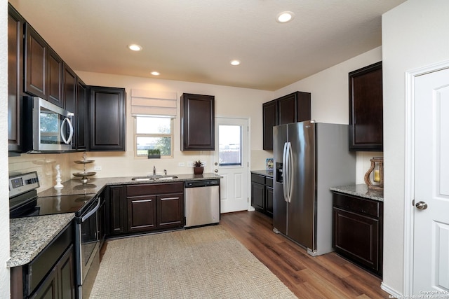 kitchen with light stone countertops, sink, hardwood / wood-style floors, dark brown cabinets, and appliances with stainless steel finishes