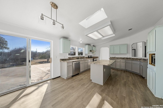 kitchen with lofted ceiling with skylight, appliances with stainless steel finishes, decorative light fixtures, a kitchen island, and wood-type flooring