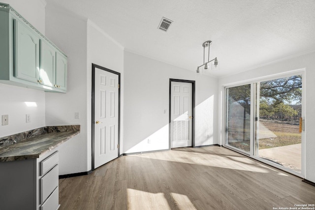 unfurnished dining area featuring a textured ceiling, light hardwood / wood-style floors, and ornamental molding