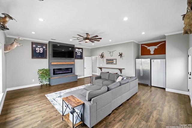 living room featuring ceiling fan, a large fireplace, wood-type flooring, and crown molding