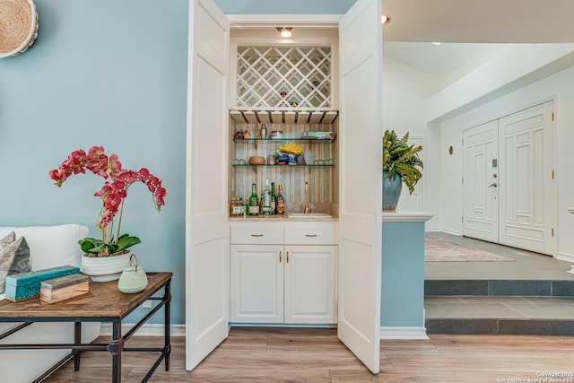 bar featuring white cabinets, light hardwood / wood-style flooring, and sink