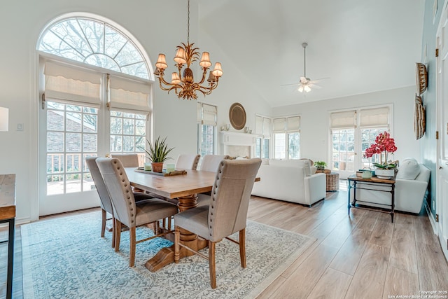 dining space featuring high vaulted ceiling, ceiling fan with notable chandelier, light hardwood / wood-style floors, and a wealth of natural light