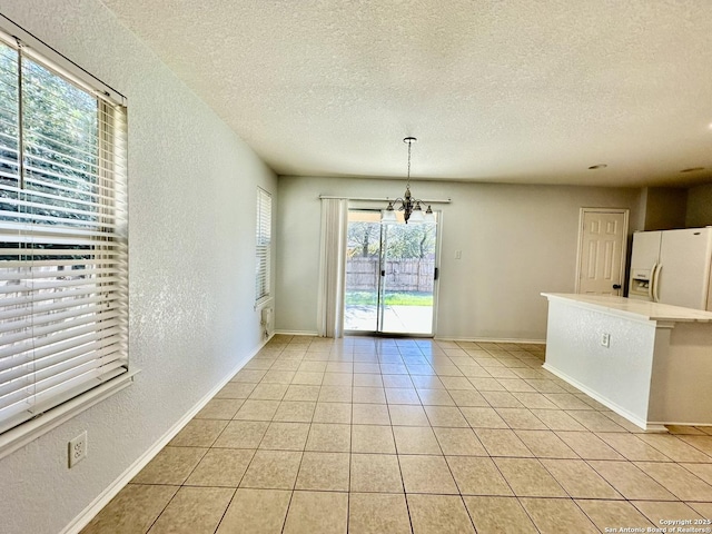 unfurnished dining area with light tile patterned floors, a textured ceiling, and an inviting chandelier