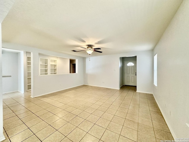 empty room with built in shelves, light tile patterned floors, and ceiling fan