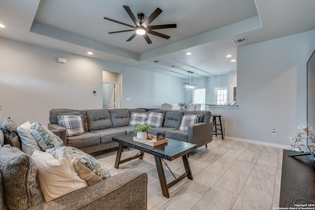 living room with ceiling fan with notable chandelier and a tray ceiling