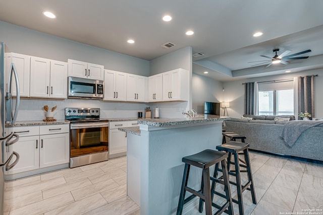 kitchen with a kitchen breakfast bar, white cabinetry, kitchen peninsula, and appliances with stainless steel finishes