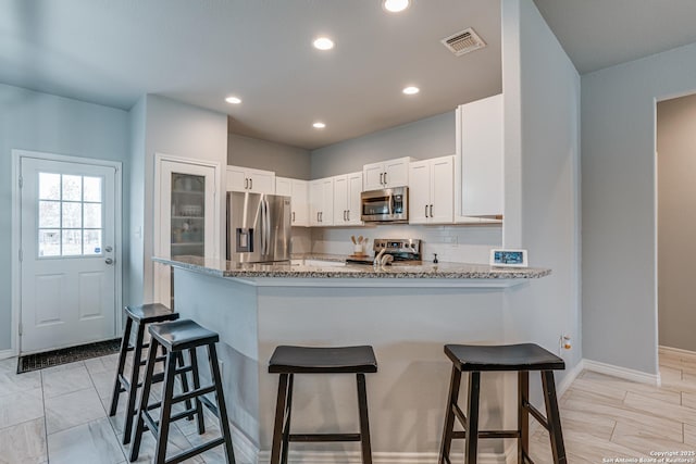 kitchen featuring white cabinetry, stainless steel appliances, tasteful backsplash, light stone counters, and kitchen peninsula