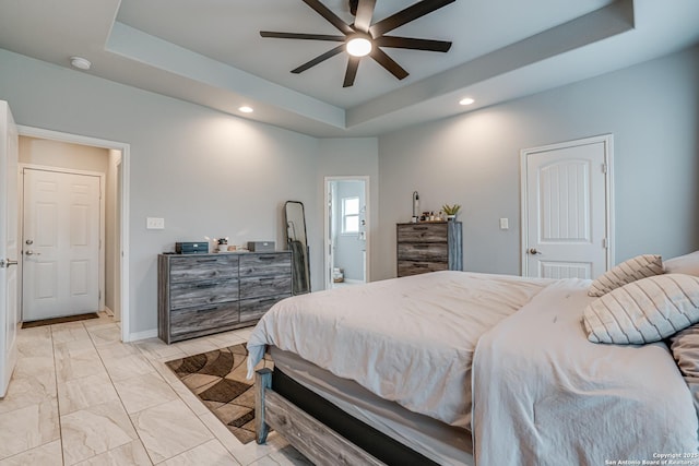 bedroom with ceiling fan, ensuite bath, and a tray ceiling