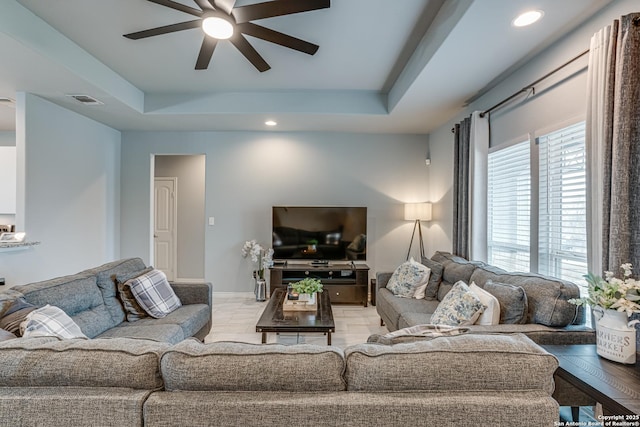 living room with a tray ceiling, a wealth of natural light, and ceiling fan