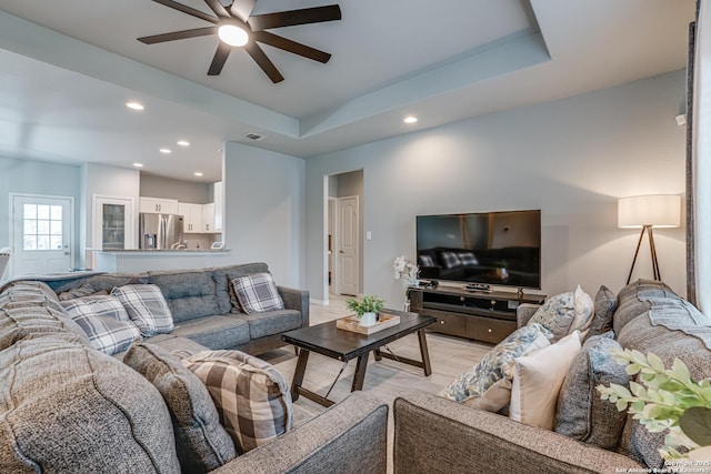 living room with ceiling fan, light hardwood / wood-style floors, and a tray ceiling