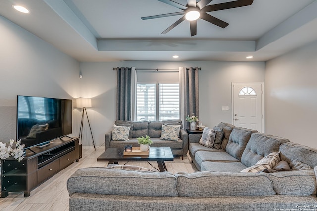 living room featuring light hardwood / wood-style flooring, a raised ceiling, and ceiling fan