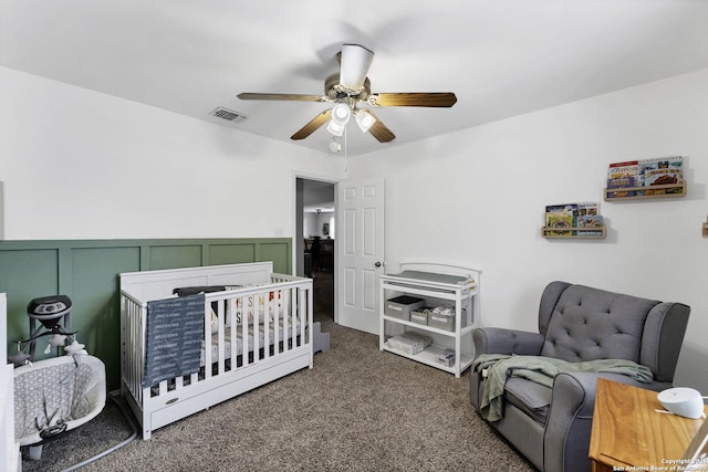 bedroom with ceiling fan, a crib, and dark colored carpet