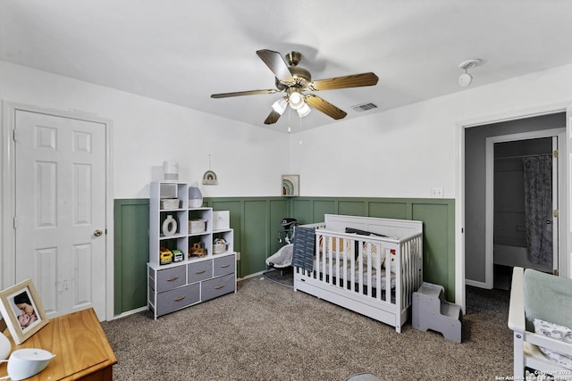 carpeted bedroom featuring a crib and ceiling fan