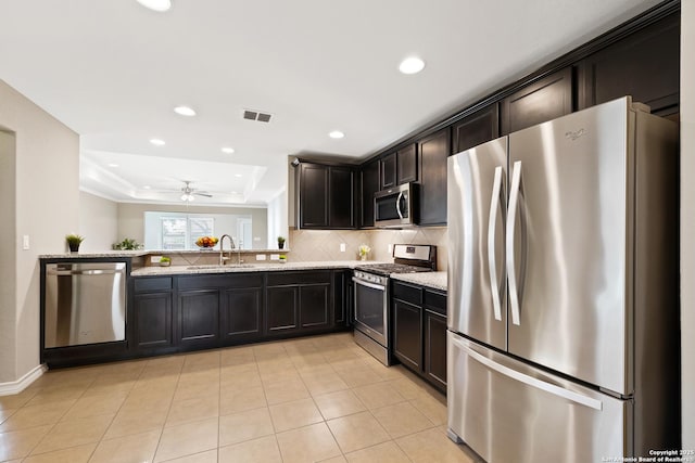 kitchen featuring sink, ceiling fan, light stone countertops, appliances with stainless steel finishes, and a tray ceiling