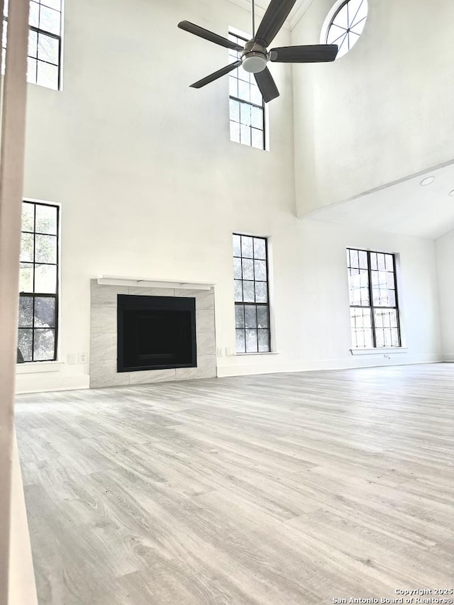 unfurnished living room featuring a wealth of natural light, ceiling fan, light wood-type flooring, and a tile fireplace