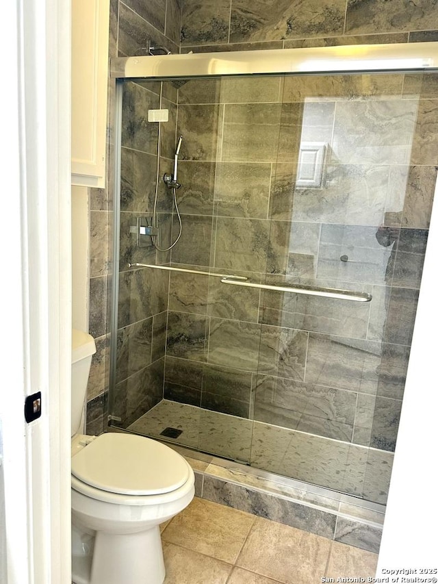 bathroom featuring tile patterned flooring, toilet, and a shower with door