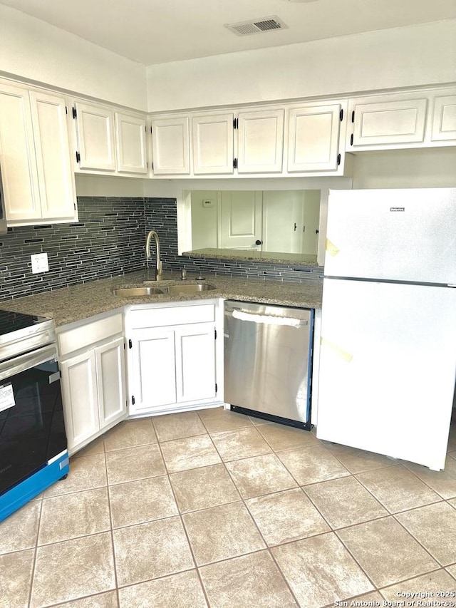 kitchen featuring white appliances, sink, light tile patterned floors, dark stone countertops, and white cabinetry