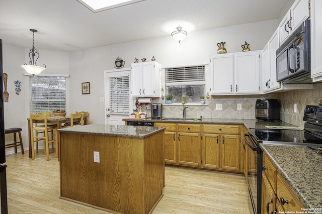 kitchen with black appliances, white cabinets, dark stone countertops, light wood-type flooring, and a kitchen island