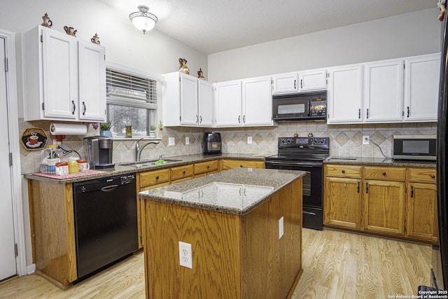 kitchen featuring light stone counters, sink, black appliances, a center island, and white cabinetry