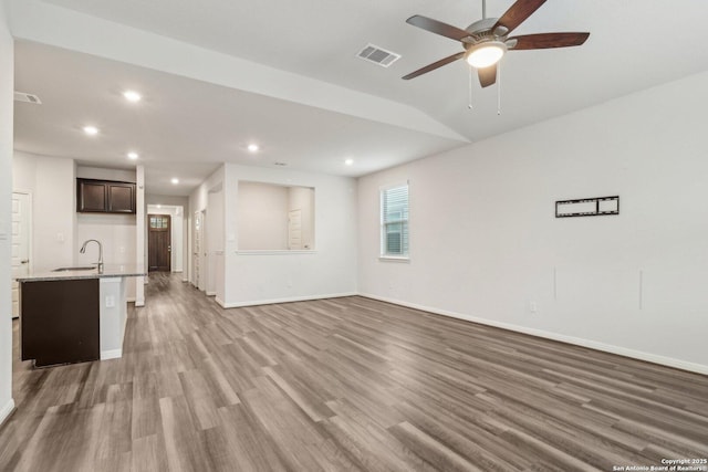 unfurnished living room featuring hardwood / wood-style floors, vaulted ceiling, ceiling fan, and sink