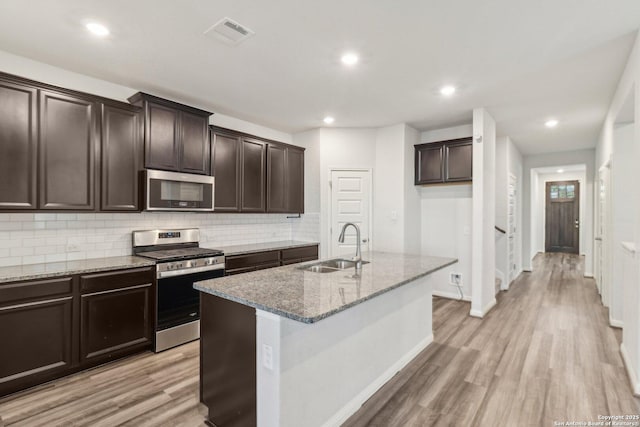 kitchen featuring a center island with sink, sink, light hardwood / wood-style flooring, light stone countertops, and appliances with stainless steel finishes