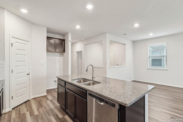 kitchen featuring dishwasher, a center island with sink, sink, light stone counters, and dark brown cabinetry